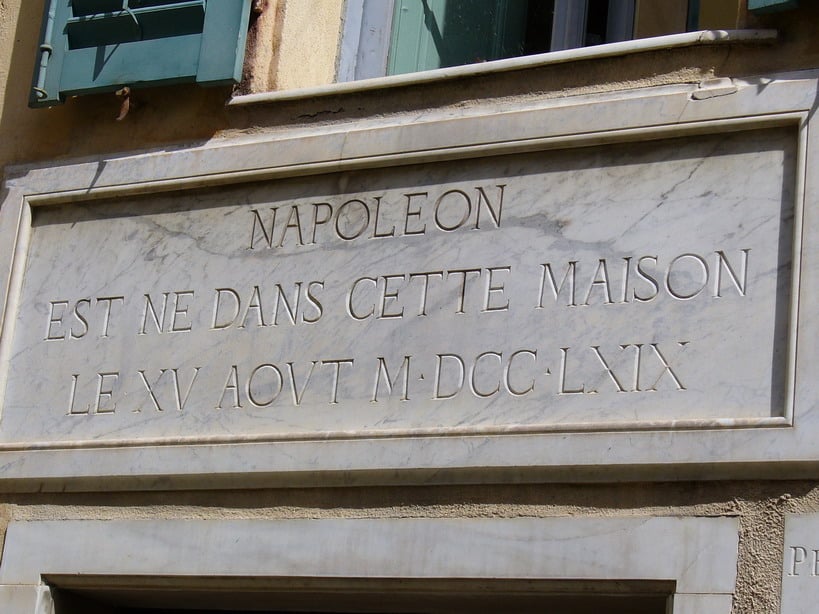 The marble plaque above the door of the Maison Bonaparte in Ajaccio, Corsica, reads "NAPOLEON | EST NE DANS CETTE MAISON | LE XV AOVT M·DCC·LXIX," which translates to "NAPOLEON | BORN IN THIS HOUSE | THE 15 AUGUST 1769.