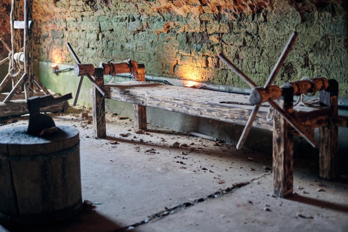 Wooden medieval torture rack with ropes and cranks in stone walled dungeon, illuminated by dim lighting, symbolizing grim reminder of historical cruelty